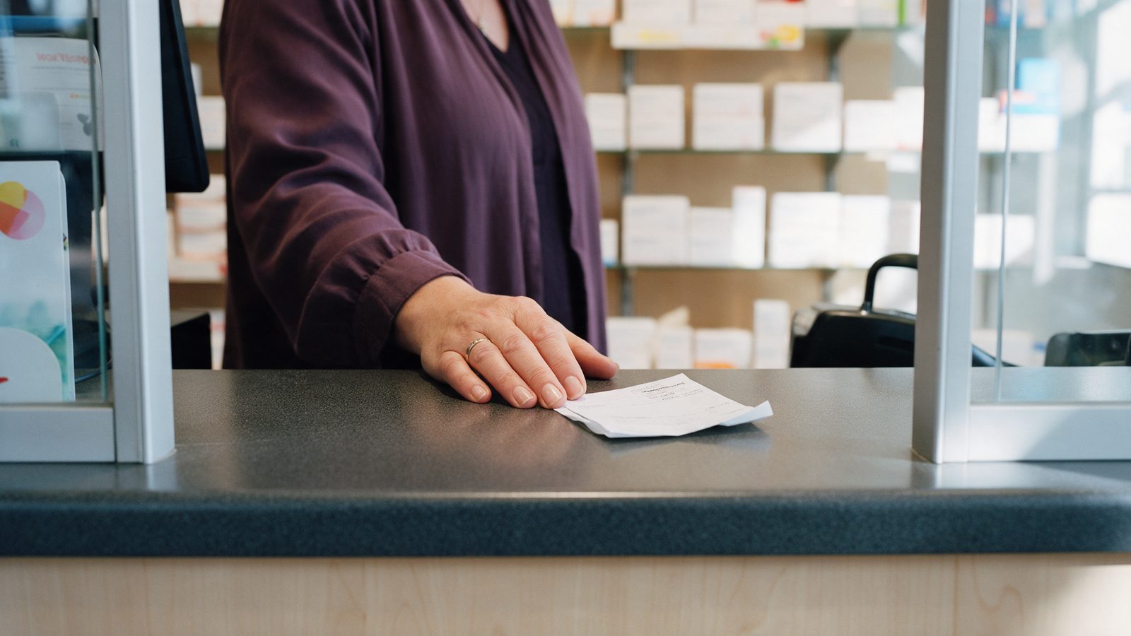 Hand van een vrouw op een apotheekbalie naast een opgevouwen papier
